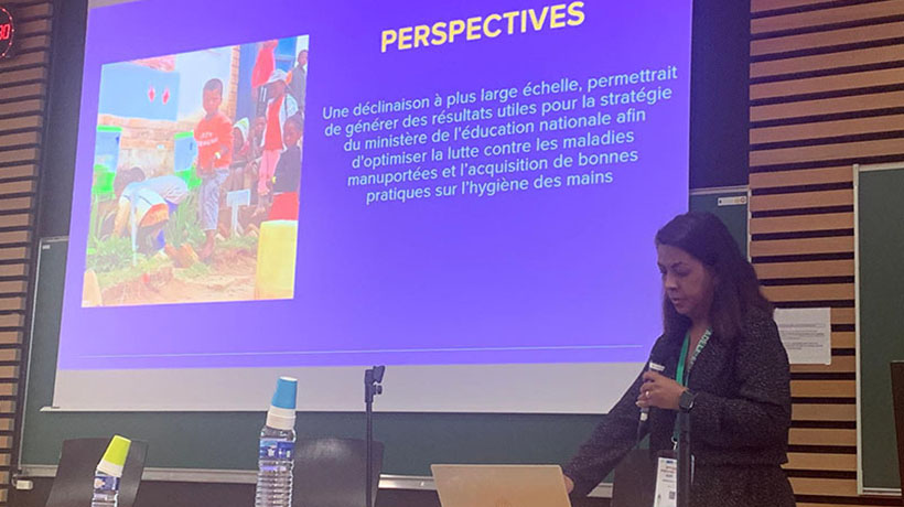 Dr Nivo Ramanamihantatsoarana, member of the Malagasy delegation present at the congress, speaks holding a microphone in front of a large screen on which a blue presentation is projected.